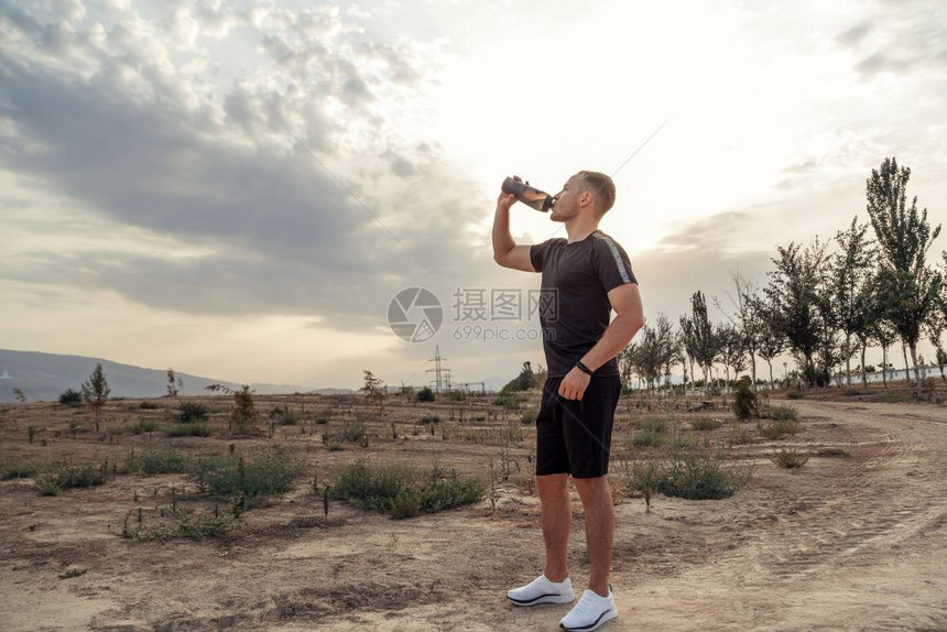 锻炼白种人慢跑者一名年轻白人男子穿着黑色T恤和短裤的肖像在培训后或前从瓶子中饮用水图片
