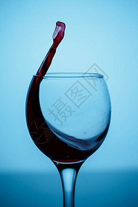 黑色的蓝背景黑光彩玻璃上杯子中的红葡萄酒喷洒运动行图片