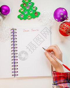 右倾木制的亲爱圣诞老人信贺卡一个拿着笔的孩子在木制背景上的白纸写字带有新年装饰童梦想的礼物新年概念亲爱的圣诞老人信贺卡一个拿着笔的孩背景