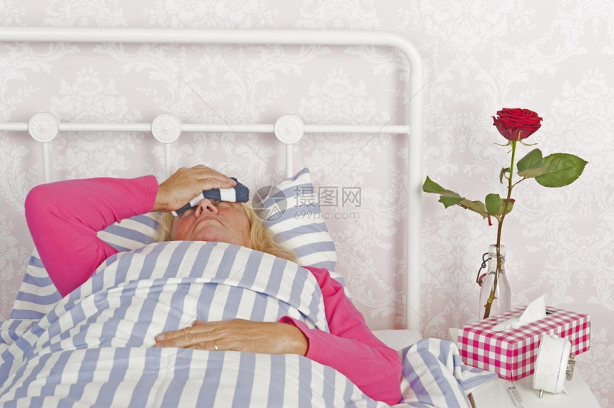 脸身穿粉红色睡衣头痛组织和一朵玫瑰的有病妇女躺在床上用毛巾着挫折悲伤图片