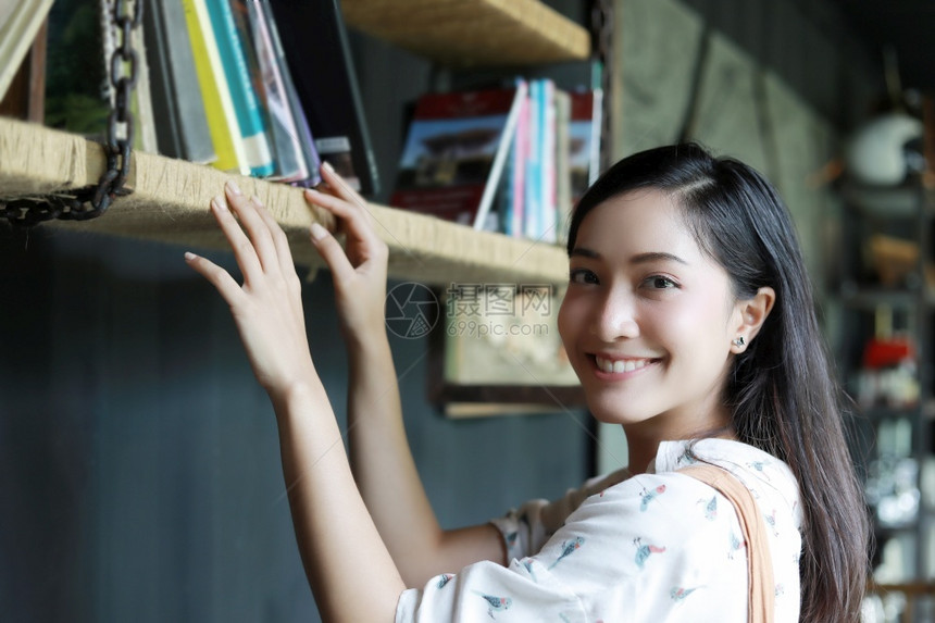 一个可爱的亚洲女人选择书架上一本的供阅读她在家度假时笑着开心为了准备学习图片
