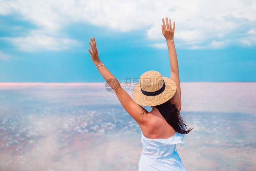乐趣一种在粉红盐湖上欢乐的快女人戴帽子的在阳光明媚的夏日在粉红盐湖上散步旅游图片