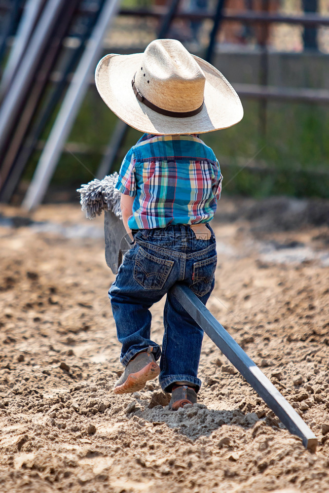 小男孩牛仔在泥土中骑着棍马与帽子可爱的西方生活式荒野年轻的一种图片