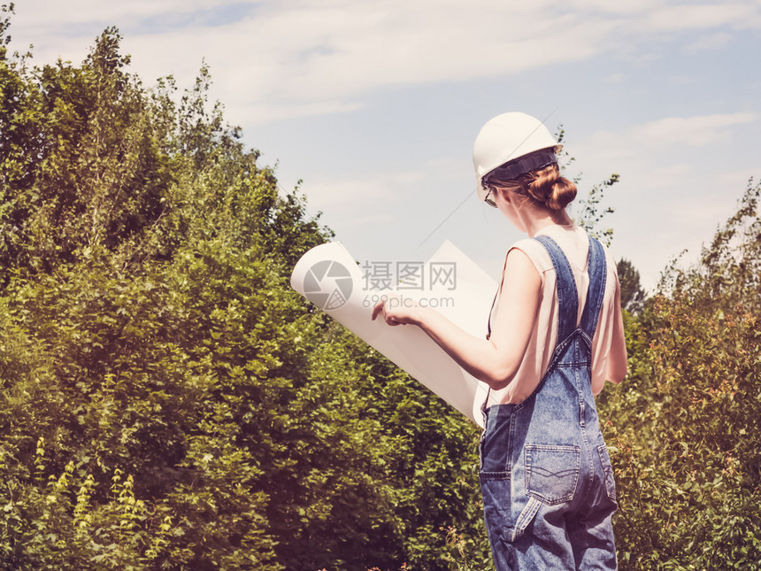 美丽的牛仔裤工程师在绿树背景下持有公园纸项目的年轻可爱女子关闭劳动和就业概念在公园持有纸项目女在公园持有纸项目以近距离劳动和就业图片