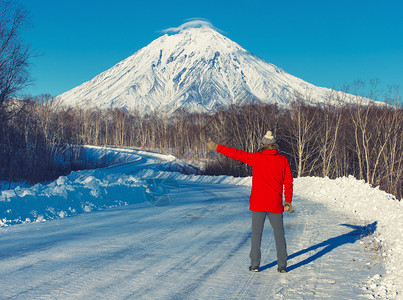 迷人的看着站在路边停车的男子面对着积雪火山的景象旅行者搭便车独奏形式图片