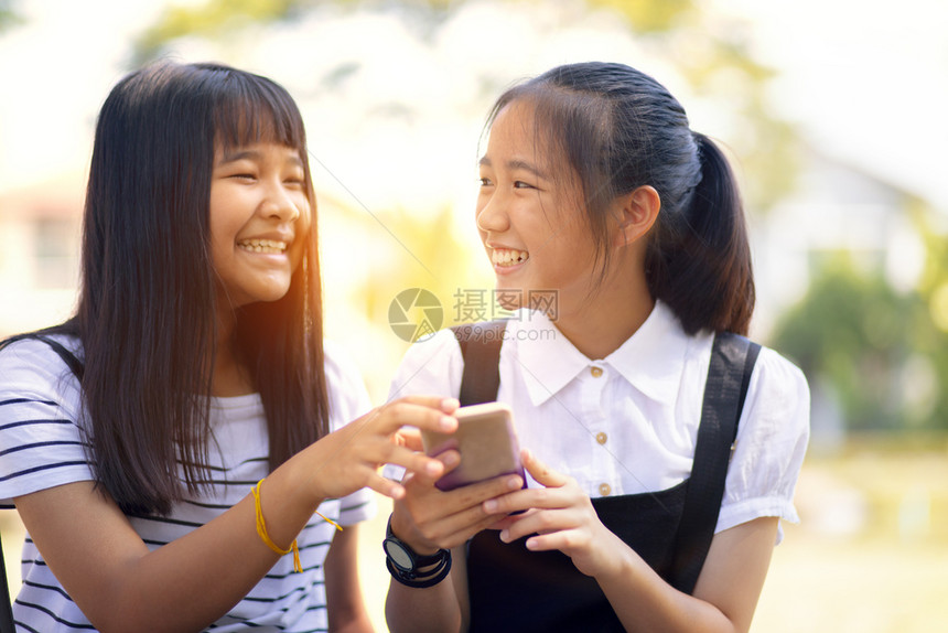 信息两个亚裔青少年笑着快乐地在智能电话屏幕上面对阅读留言幽默松弛图片
