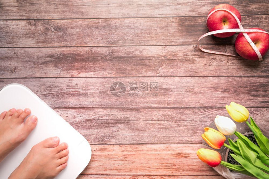 措施妇女脚站着规模饮食红苹果与木质背景健康和生活概念的测量胶带捆绑在一起木质背景上有女双脚按比例表站立和饮食红苹果男人女士图片