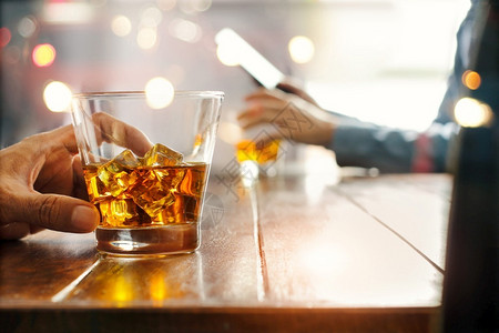 威士忌酒敬在吧前的柜台关上两个喝威士忌酒精饮料的男子手机背景图片