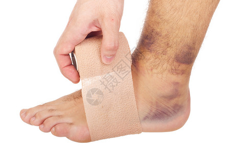痛苦扭曲的脚踝伤年轻男子用医疗绷带隔离在白色背景上治疗图片