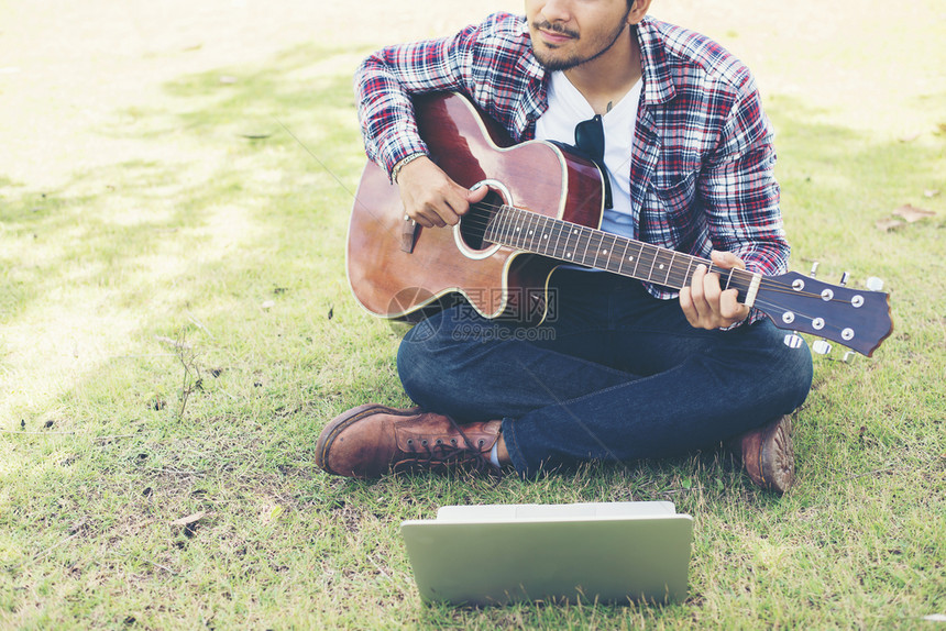 年轻时装男在公园里用笔记本电脑练习吉他快乐的青年时装男在公园里用笔记本电脑练习吉他快乐地玩旋律男歌曲图片