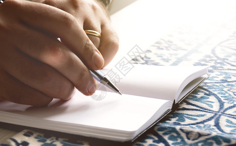 思维创想有创造力的记事本男手握一支圆点笔写在开放记本上的空白页创时灵感工作场所背景