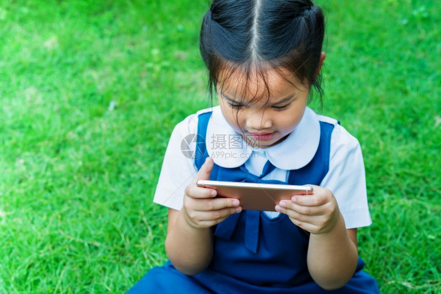 女孩们利用手机智能在草地上玩因特网的可爱小女孩微笑教育图片