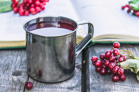 甜点木桌上的杯子或一热荚蒾茶旁边是一本打开的书和红色荚蒾浆果天然维生素的来源用于民间医学特写杯子或一热荚蒾茶放在木桌上旁边是一本图片