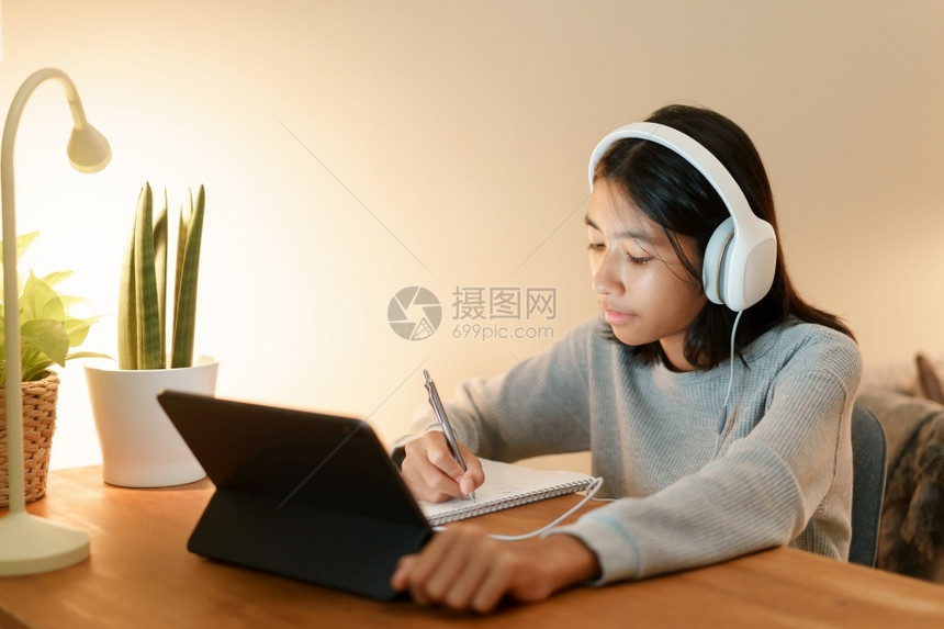 家教做庭功课的亚洲女孩和在家夜用耳机平板数字电脑上与教师一起在线学习导师孩子移动的图片