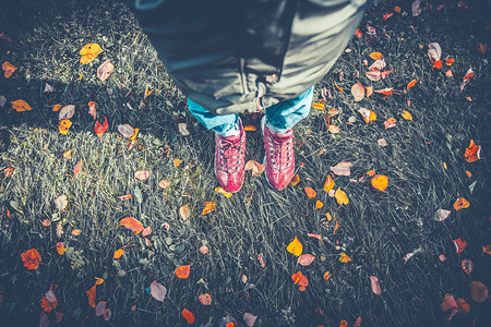 穿着运动鞋的女孩站在落叶草地上图片