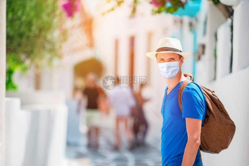 面具独自的如画身戴外科面罩的年轻人在城市空旷街道上面临保护的他们带着背负包的青年男子行走欧洲老城的背景是自拍图片