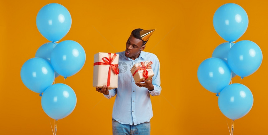 庆祝时尚带着两个红丝的礼物盒黄色背景微笑的男得到惊喜活动或生日庆典气球装饰盛着礼品盒的欢快男子生日等并拥有一个惊喜事件或生日庆典图片