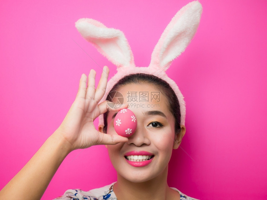 四月春天丰富多彩的复活节时戴兔子耳朵头带和携复活节鸡蛋的妇女有吸引力的年轻女在明亮的粉红背景上微笑图片
