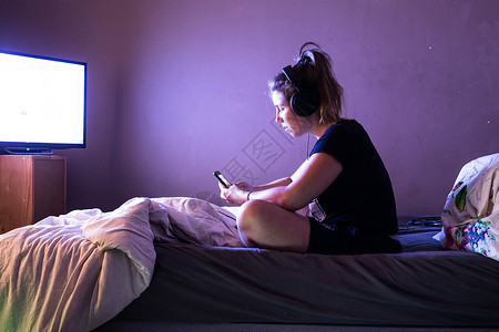 若影若现肖像娱乐年轻女子晚上在床看电视十几岁的女孩在她现代卧室里戴着耳机和数字平板电脑在黑暗中年轻女子在晚上床看电视影十几岁的女孩在她现背景