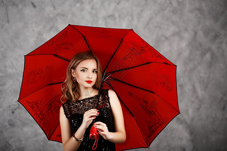 身着黑色晚礼服和红伞式雨的年轻姑娘身着红色伞式雨的年轻女士孩吸引人的图片