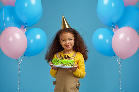 甜的女oopicapi戴帽子的有趣小女孩拿着生日蛋糕蓝背景的色漂亮的女孩得到了一个惊喜活动庆祝气球装饰戴着帽子的有趣小女孩拿着生背景图片