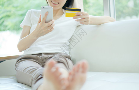 坐在沙发上笑着开心地坐的平板电脑和信用卡购物妇女亚洲人数字的长椅图片