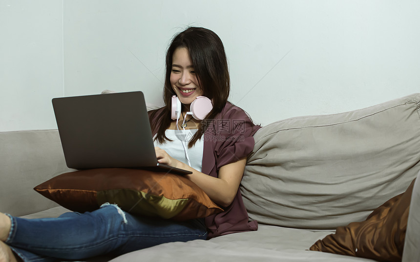 活的肖像人使用笔记本电脑和耳机的亚洲年轻美女在家用生活风格技术和新常识概念客厅休息时使用笔记本电脑和耳机图片