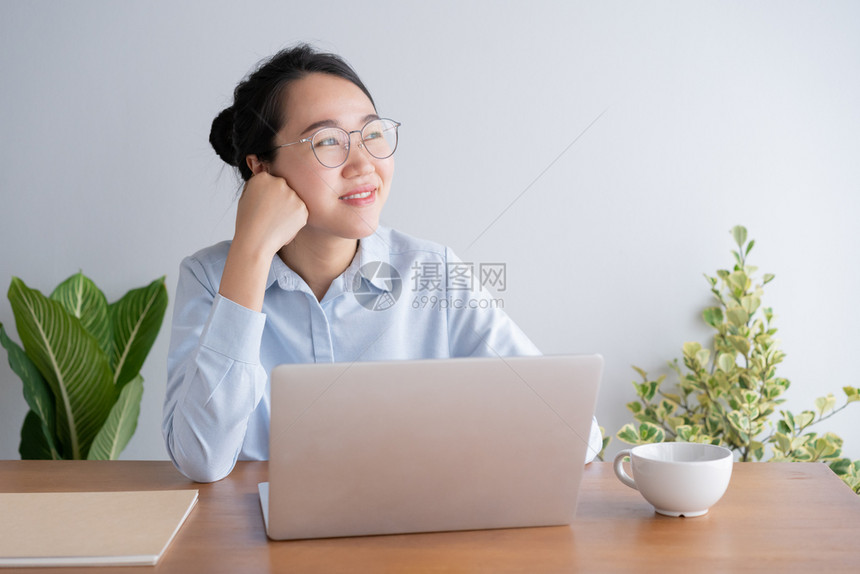 女商人在办公室桌做笔记本电脑工作的年轻亚洲妇女坐在桌子上手靠着下巴躺公司的随意图片
