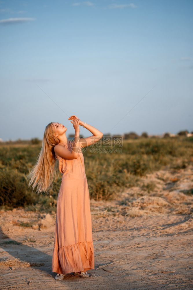 一位年轻美丽的白人金发女肖像穿着粉红裙子在荒野中面对日落华丽的淑女摆姿势图片