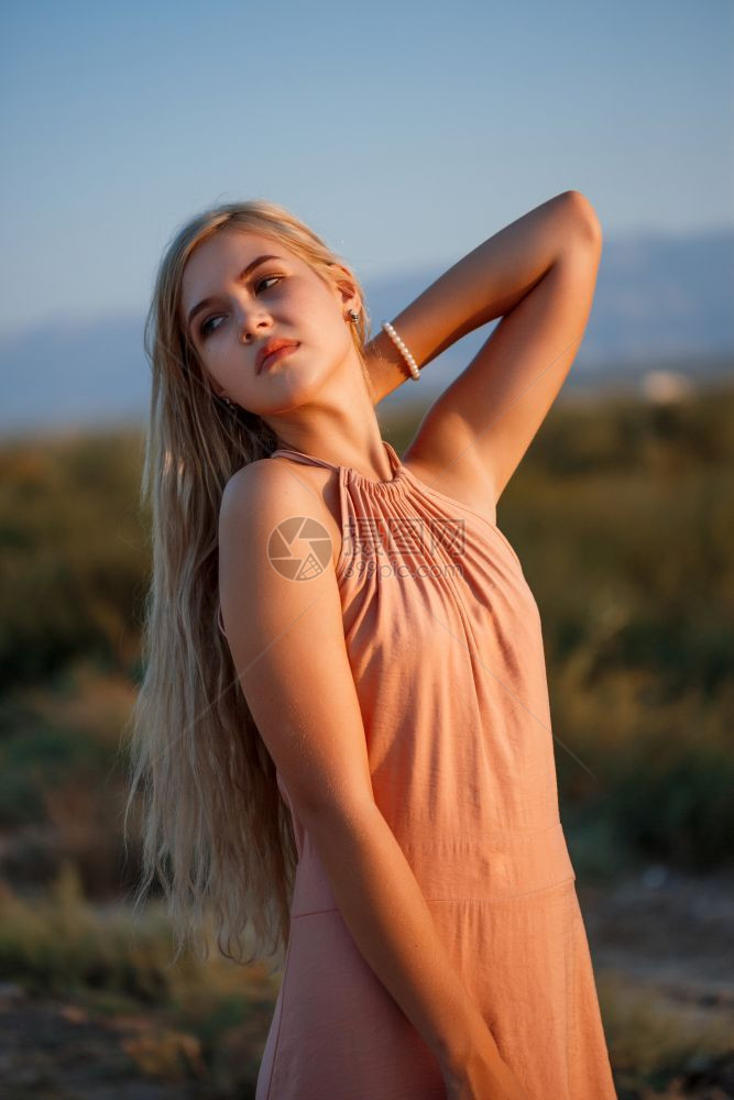 女孩一位年轻美丽的白人金发女肖像穿着粉红裙子在荒野中面对日落吸引人的头发图片