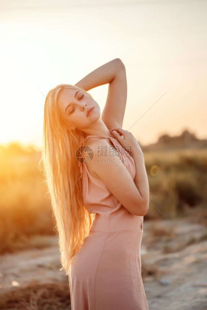 时髦的一位年轻美丽白人金发女肖像穿着粉红裙子在荒野中面对日落常设户外图片