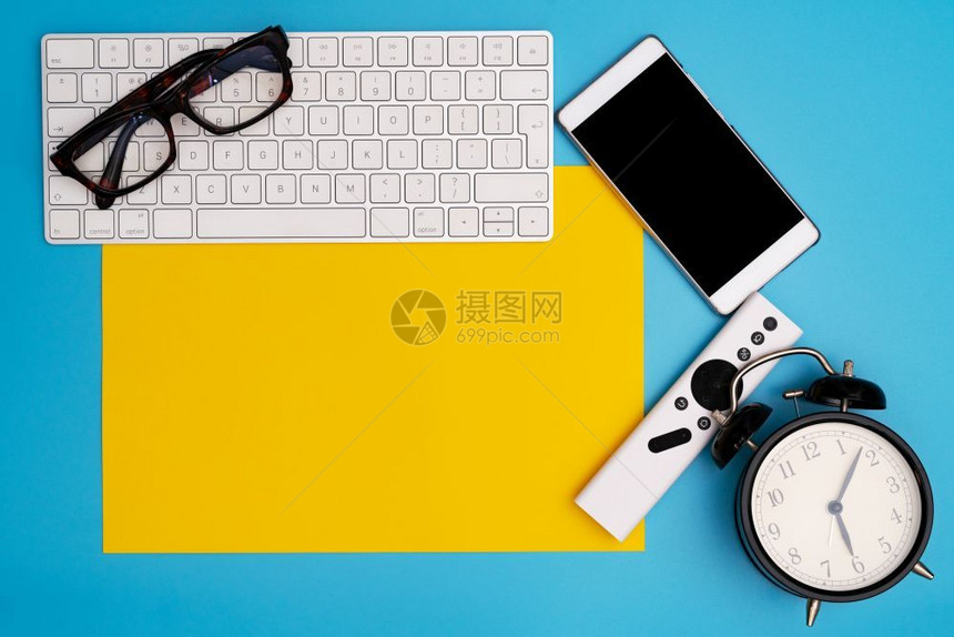 带有计算机键盘眼镜智能手机和时钟顶视复制空间的黄色纸复印空间电话桌上有创造力的图片