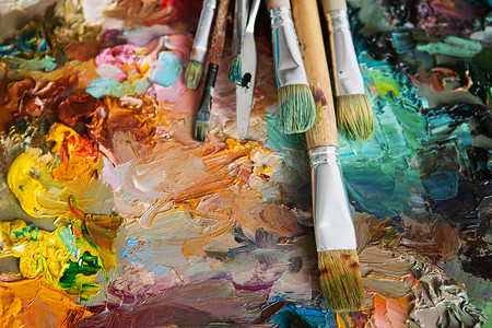 工艺术家在木制调色盘上刷子和涂油画大型艺人调味盘不同颜色的质料混合油漆以及用笔和调色板加颜料味丰富多彩的抽象背景图片