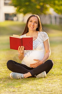 Caucasian孕妇在绿地一书上阅读的照片公园微笑健康图片