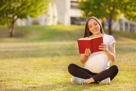 母亲晴天外部Caucasian孕妇在绿地一书上阅读的照片图片