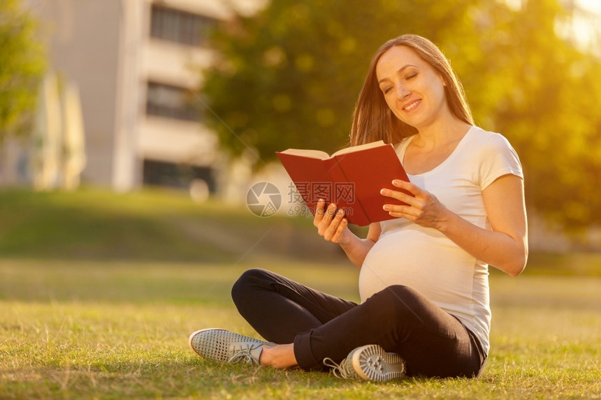 怀孕黑发外部妇的照片正在阅读一本关于绿地的书图片