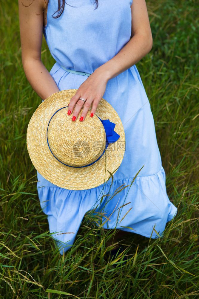 田野里穿着蓝色连衣裙的漂亮女孩手里拿着一顶帽子田野里穿着蓝色连衣裙的漂亮女孩手里拿着一顶帽子浪漫的健康黄色图片