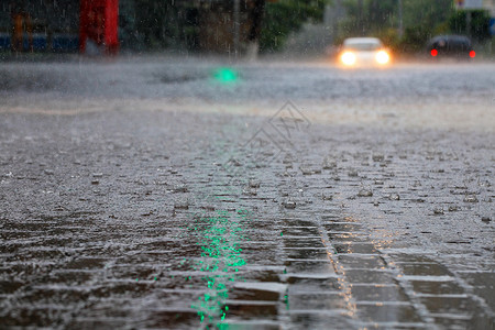 滂沱湿的车头灯光照亮了人行道和沥青路上的大雨路口的绿色交通灯照亮了汽车光路口的绿色交通灯光照亮了城市街道上的大滴子和一条水流背景