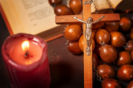 十字架上的耶稣崇拜祈祷与红蜡烛和圣经书精神氛围宗教概念交叉的大木罗萨里珠子和智慧背景