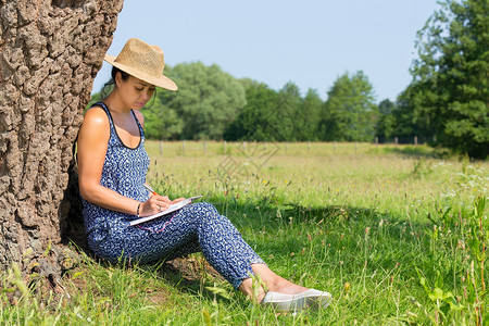 树木舍内维尔春天坐在树干旁写草地的年轻女士图片
