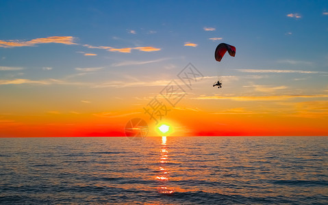 逃离活动行日落时海上和滑翔伞日落时飞越海面的滑翔翼背景图片