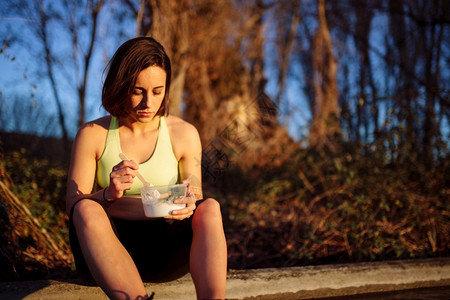 喝赛跑者食物日落时在田里吃健康午餐的年轻运动妇女图片
