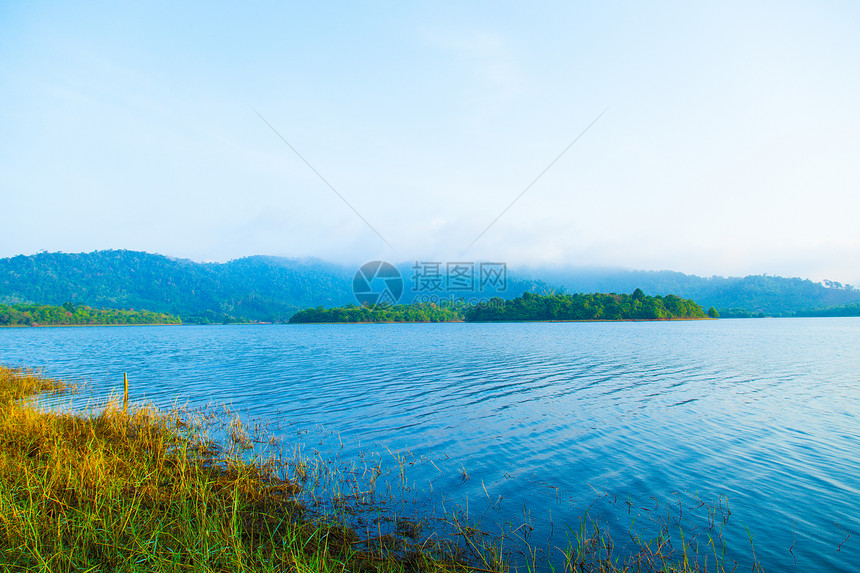 草自然岛屿湖和山丘覆盖着森林和浓雾在清晨反射图片