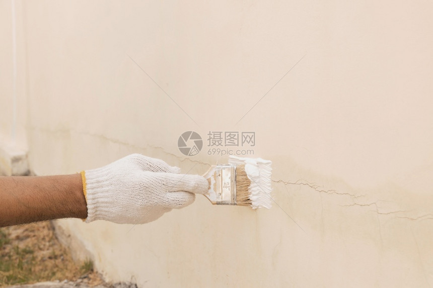 男人转换健康用白布手套来改造油漆以封住水泥墙上的裂缝使用白布手套将涂料改漆以密封混凝土墙上的裂缝图片
