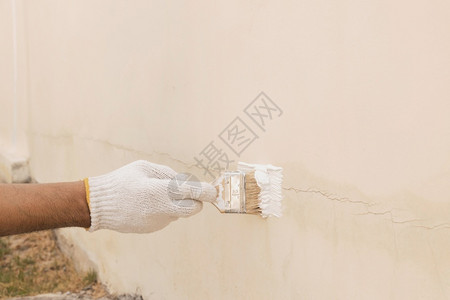 男人转换健康用白布手套来改造油漆以封住水泥墙上的裂缝使用白布手套将涂料改漆以密封混凝土墙上的裂缝背景