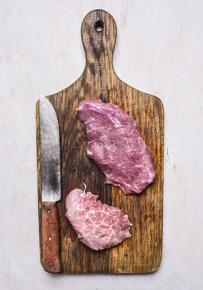 新鲜的生猪肉牛排用刀子在旧剪切板上白色背景最美饮食烧烤木板图片