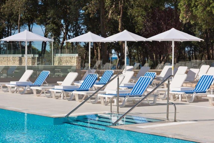 阳光明媚的一天带游泳池梯子的阳床和雨伞栏杆椅子蓝色的图片