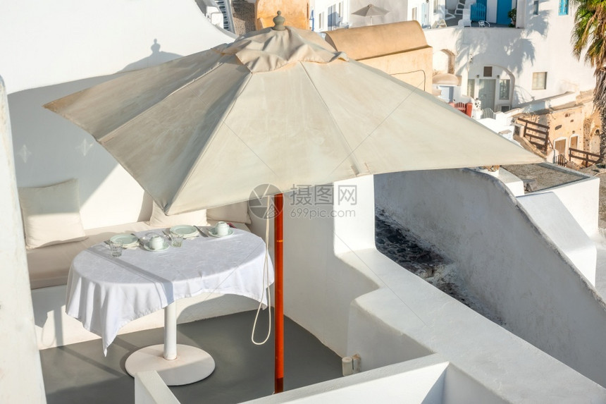 海滨田园诗般的奢华在圣托里尼岛卡路德拉的希腊阳光夏日天在圣托里尼岛的一个伞状平台下在露天梯田地服务表上配有桌布和雨伞在圣托里尼岛图片