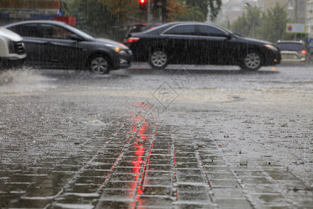 下雨滂沱人行横道路和上的暴风雨路过汽车的人行道上喷着由红色交通灯光照亮的横雨人行道上的大雨和沥青路被红交通灯照亮背景图片