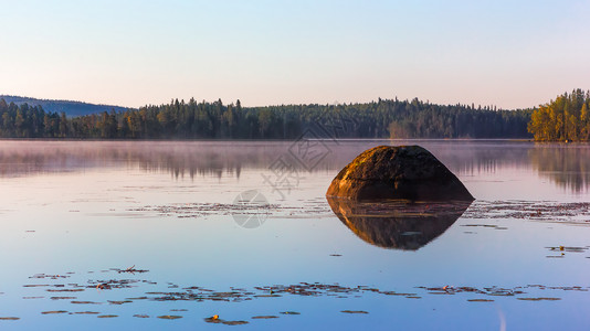 雾气弥漫的湖面反射的森林和巨大的石头图片